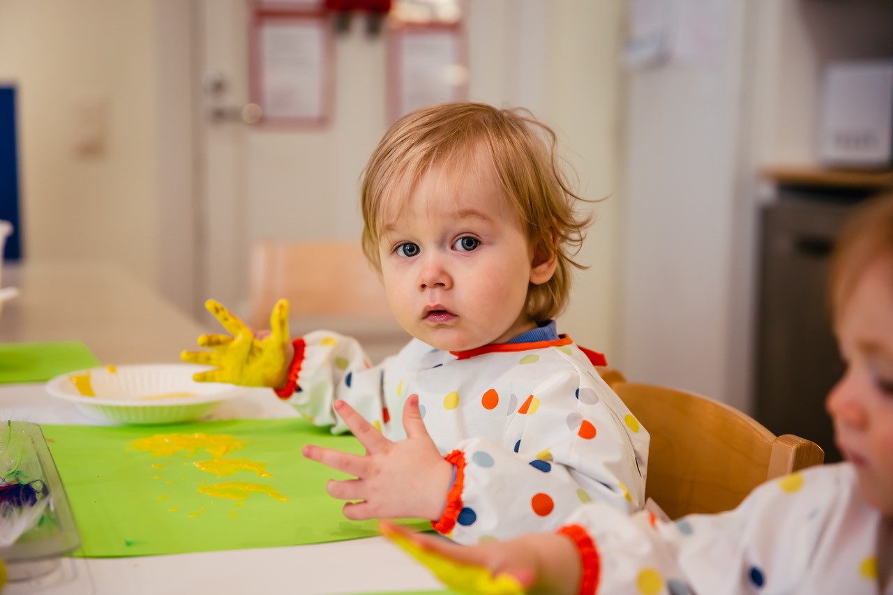 Päiväkotilapsi leikkii sormiväreillä pöydän äärellä.